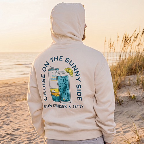 Sun Cruiser Jetty collaboration hoodie on a man in front of beach dunes during sunset.