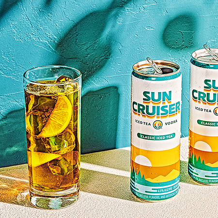 A portrait of cans of Sun Cruiser next to a full glass of Sun Cruiser Classic Iced Tea