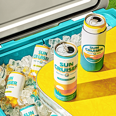 Cans of Sun Cruiser on a table with a cooler full of ice and Sun Cruisers behind